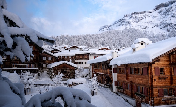 Snow-covered Swiss chalet in winter wonderland with snow-laden pine trees and mountain backdrop